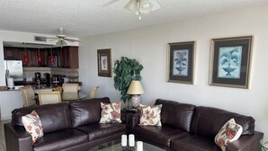 A living room with a dark brown leather sectional sofa, a glass coffee table, and a dining area in the background.