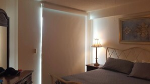 A bedroom with a bed, a nightstand with a lamp, a dresser, and a painting on the wall.