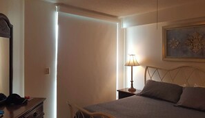 A bedroom with a bed, a nightstand with a lamp, a dresser, and a painting on the wall. - Luxuroius Oceanfront Condo, Garden City Beach, Wifi, AC, Cable TV, Pool, Jacuzzi (Murrells Inlet)