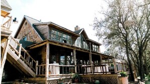Ein großes, rustikales Holzhaus mit einer breiten Veranda und zahlreichen Fenstern.