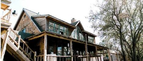A large, rustic wooden house with a prominent porch and multiple windows.