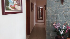 Un pasillo con una pared de piedra, un cuadro enmarco de un barco y un jarrón de flores.