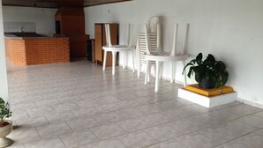 Una habitación amplia con piso de baldosas, chimenea de ladrillo, sillas blancas y una pequeña mesa con una planta en maceta.