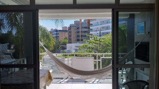 Un balcón abierto con una hamaca, una mesa con mantel floreado y vistas a edificios y follaje.