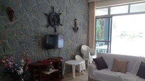 Una sala de estar con pared de piedra, televisor montado, sofá blanco, una mesita y una planta en maceta.
