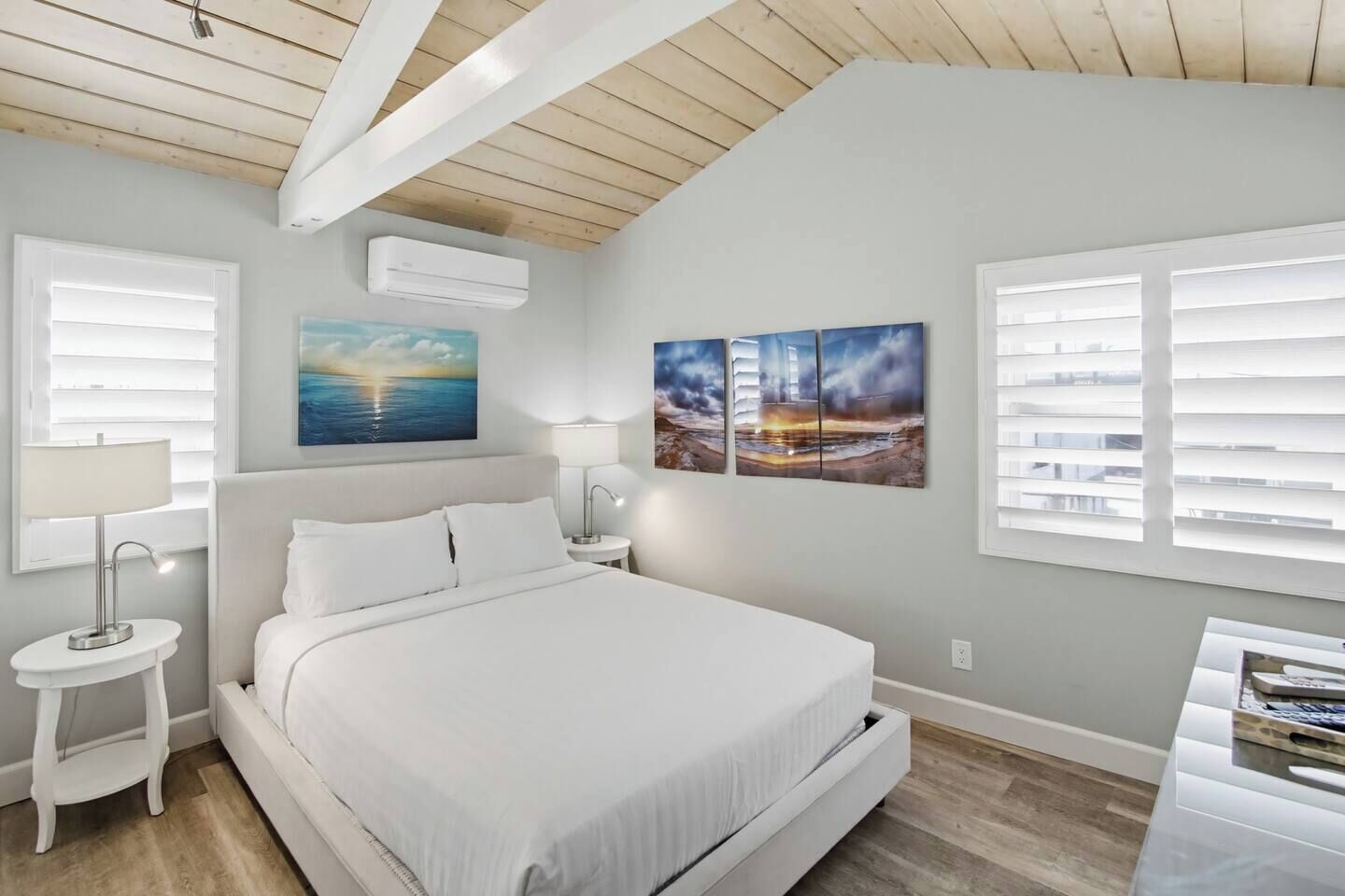 Un dormitorio con cama, dos mesitas de noche, un aparador, aire acondicionado de pared y una ventana con persianas.