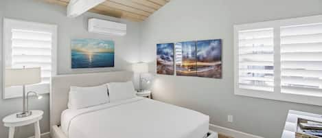 Un dormitorio con cama, dos mesitas de noche, un aparador, aire acondicionado de pared y una ventana con persianas.