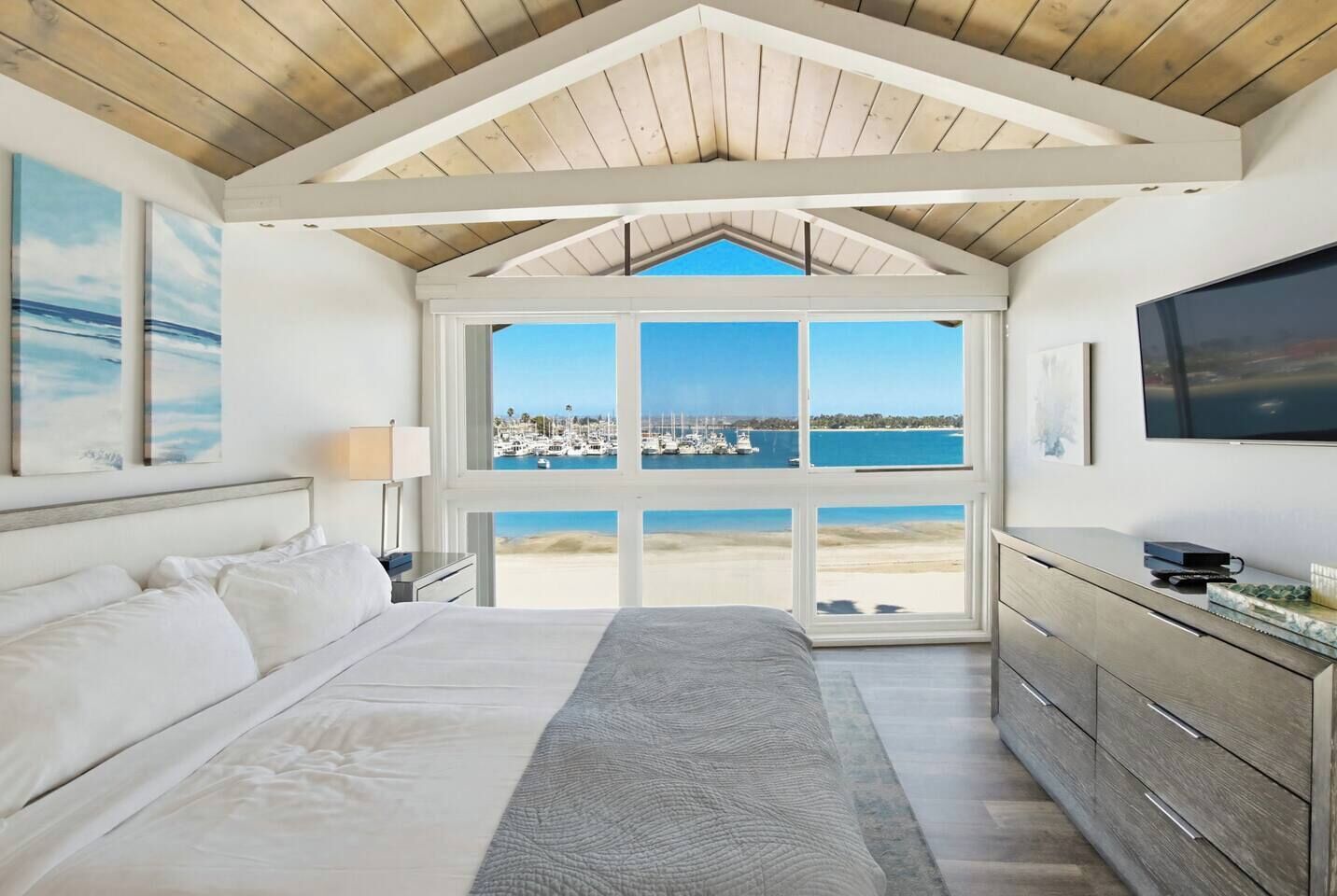Slaapkamer met een groot bed, een televisie en uitzicht op de jachthaven en het strand.