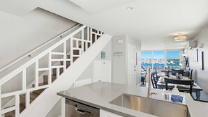 Eine moderne Küche mit Geschirrspüler aus Edelstahl, einer weißen Treppe und einem Essbereich mit Blick auf den Hafen.