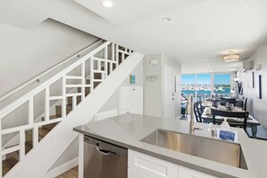 A modern kitchen with a stainless steel dishwasher, a white staircase, and a dining area with a view of the marina.