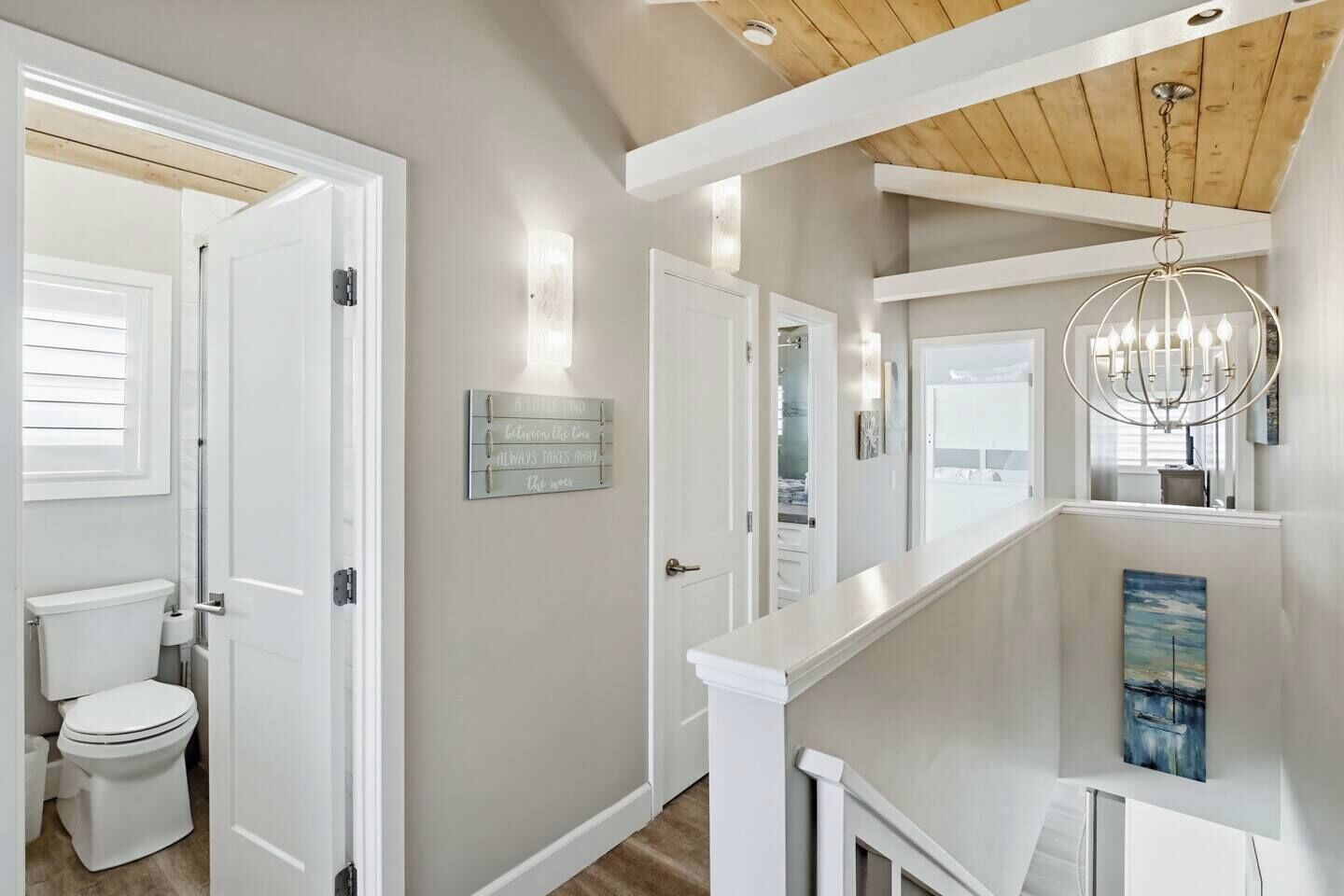 A hallway with a white door leading to a bathroom, a light fixture, and a painting on the wall.