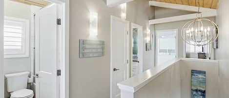A hallway with a white door leading to a bathroom, a light fixture, and a painting on the wall.