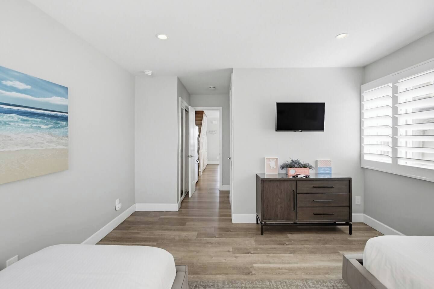 Une chambre à coucher comprenant un lit, une commode, un téléviseur et une fenêtre avec des stores.