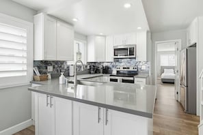 A modern kitchen with white cabinetry, a central island, stainless steel appliances, and a view to the adjacent bedroom. - Beautiful Bayfront views! Townhome for family fun (San Diego)