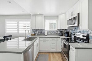 Una cocina moderna con muebles blancos, una isla central, electrodomésticos de acero inoxidable y una ventana con persianas.