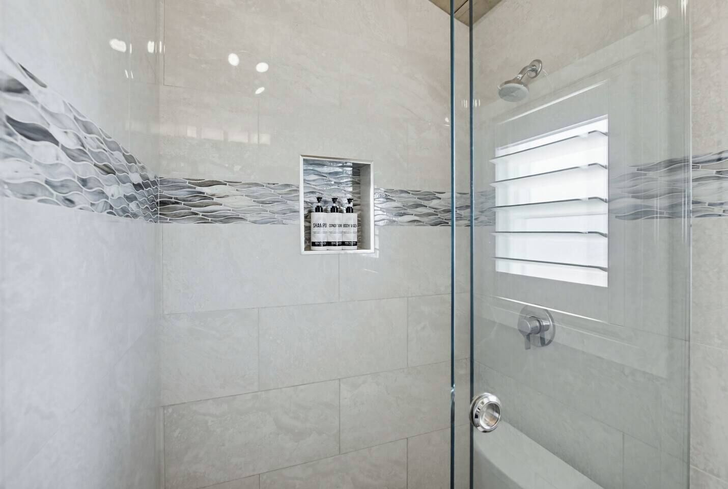 Eine gläserne Dusche mit gefliesten Wänden, einer Duschbrause und einer Glastür mit Griff.