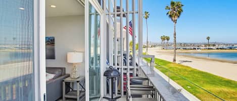 A balcony with a view of the beach, a table with chairs, and a flag.