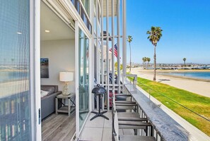 A balcony with a view of the beach, a table with chairs, and a flag.
