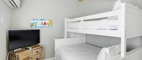 A bunk bed room with a television on a wooden dresser, white bedding, and a painting on the wall.