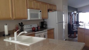 A kitchen with wooden cabinets, a white microwave, a stainless steel refrigerator, a stove, and a sink. - Desert Escape Vacation Rental (Chandler)