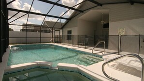 Ein Hallenbad mit klarem Wasser, umgeben von einer Glaskonstruktion, mit Liegestühlen und einem Whirlpool.