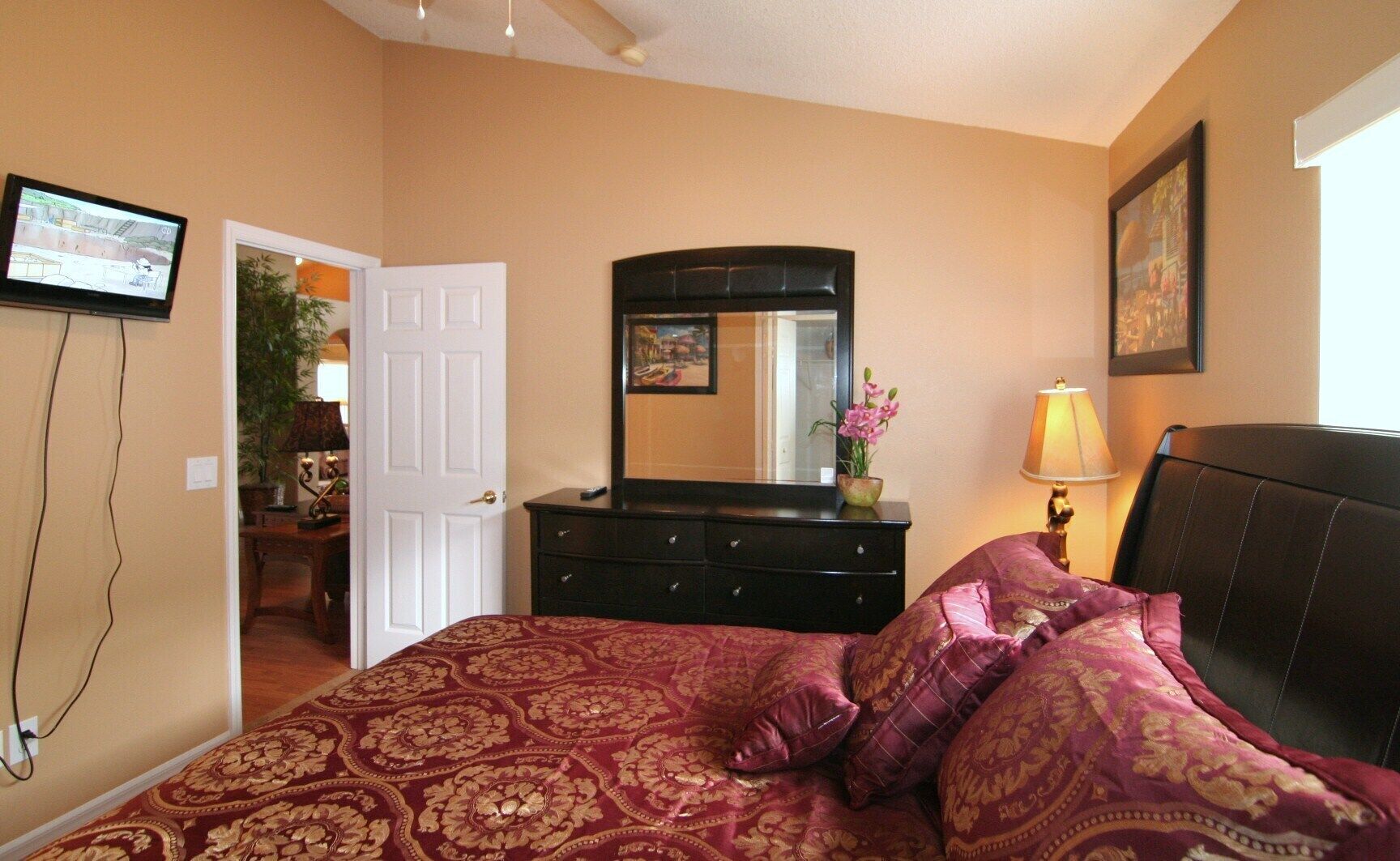 A bedroom with a large bed, a dresser, a mirror, a lamp, and a television.