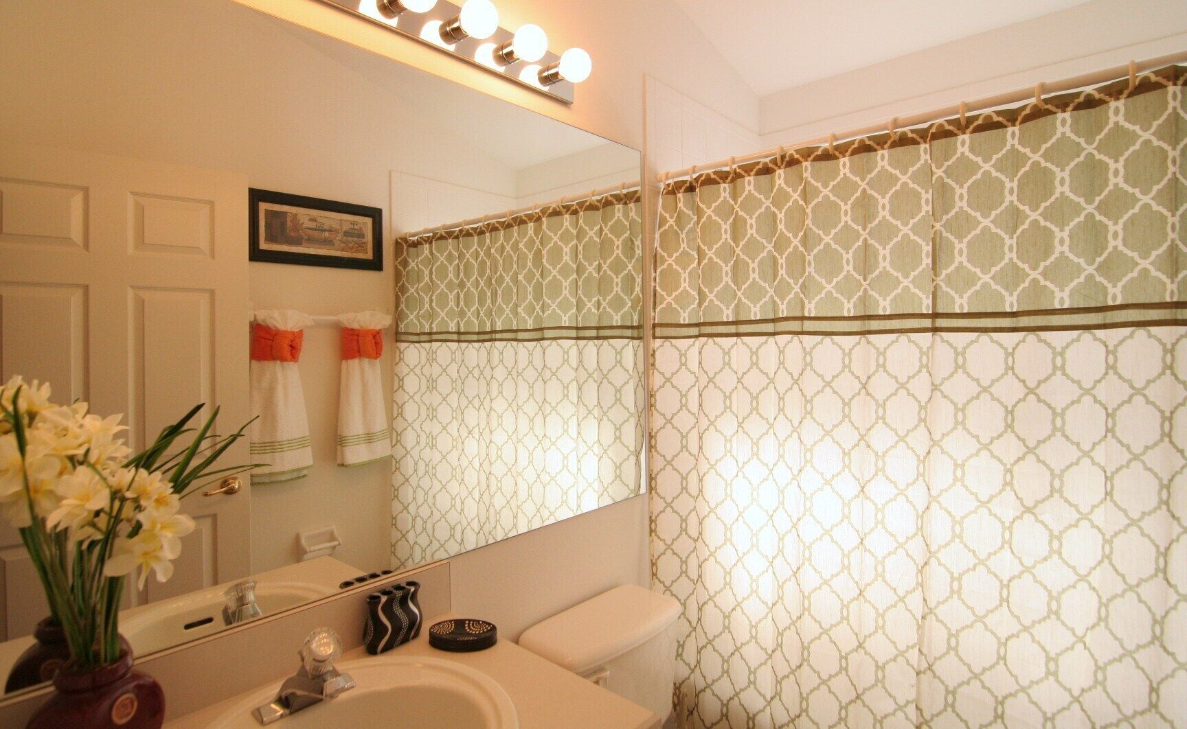 A bathroom with a white sink, mirror, and vanity, a toilet, and a shower curtain with a geometric pattern.