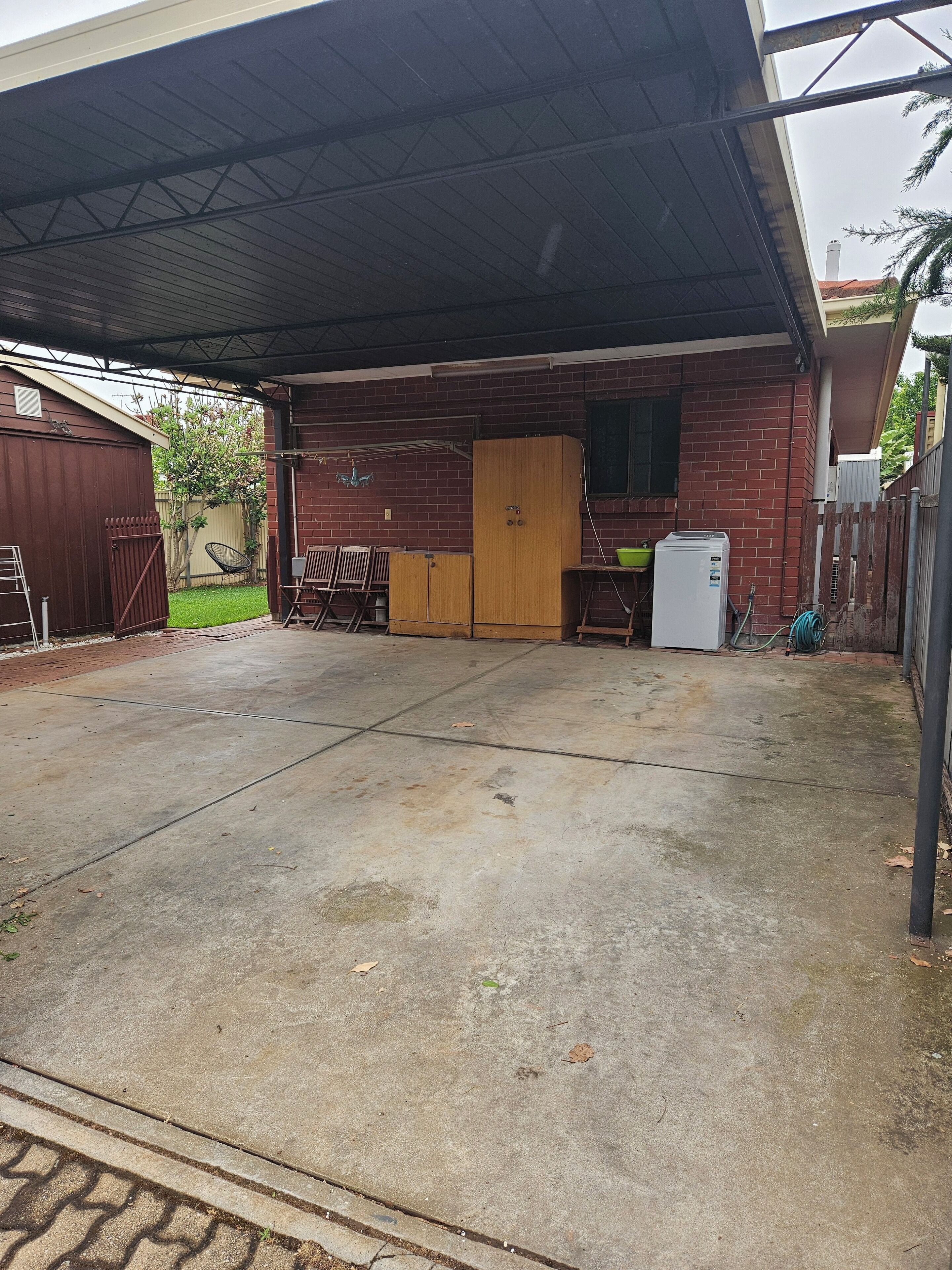 A covered outdoor area with a brick building, a wooden door, and a small white refrigerator.