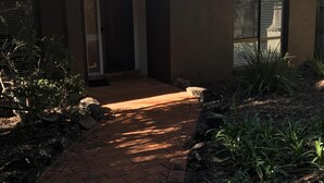 Una casa con un sendero de ladrillos que conduce a la puerta principal, rodeada de vegetación y palmeras.