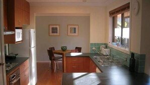 Cocina compacta con armarios de madera, un refrigerador, una mesa de comedor con sillas y una ventana con persianas.