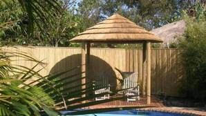 Una piscina con un pabellón de techo de paja y dos sillas.