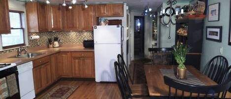 Una cocina con armarios de madera, un refrigerador blanco, una mesa de comedor con sillas y una araña.