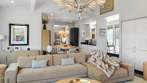 Un salon moderne avec un canapé d’angle beige, une table basse ronde et un lustre.