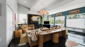 Un salon moderne avec un grand canapé, une table basse et une cheminée. Les murs sont ornés de tableaux encadrés et un lustre est suspendu au plafond.