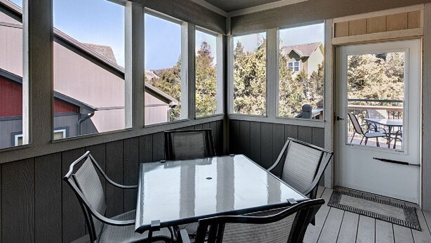 Une véranda avec une table et des chaises en verre, de grandes fenêtres et un ventilateur de plafond.
