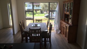 Zona pranzo con tavolo apparecchiato per quattro persone, un mobiletto in legno e vista all'esterno tramite una porta in vetro.