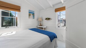 Een slaapkamer met een groot bed, een nachtkastje met een lamp, een raam met uitzicht en een kleine tafel met een plant.