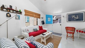 Een woonkamer met een witte bank, gestreepte kussens, een rode plaid, een houten salontafel en een rode fauteuil.