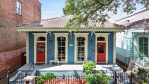 A two-story building with a red door and a blue facade, featuring a small porch and a fenced garden area. - Camelback Guest House (New Orleans)