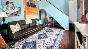 A living room with a black leather sofa, patterned rug, and a staircase leading to another room. - Camelback Guest House (New Orleans)