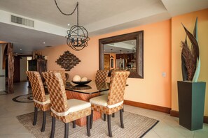 A dining area with a glass-top table, wicker chairs, a decorative wall piece, and a tall plant.