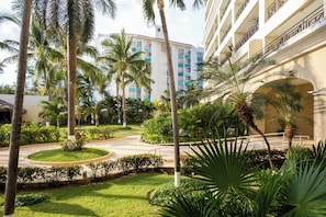A hotel courtyard with palm trees, a circular driveway, and a multi-story building with balconies.