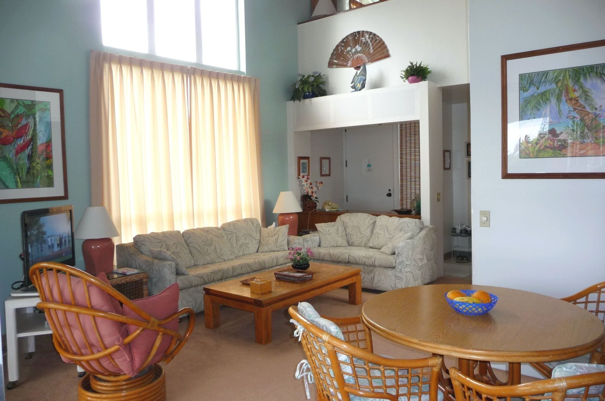 Uma sala de estar com sofá, cadeiras, mesa de centro e mesa de jantar com um cesto de frutas.