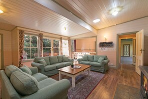 A spacious living room with two green sofas, a wooden coffee table, and a fireplace. - Glen Isla   – Blue Mountains Accommodation for 12, 6bdm Historic Blue Mountains Cottage - Sleeps 12 (Wentworth Falls)