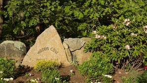 Un jardin avec un grand rocher portant l’inscription « Hidden Cove » et diverses plantes et fleurs.