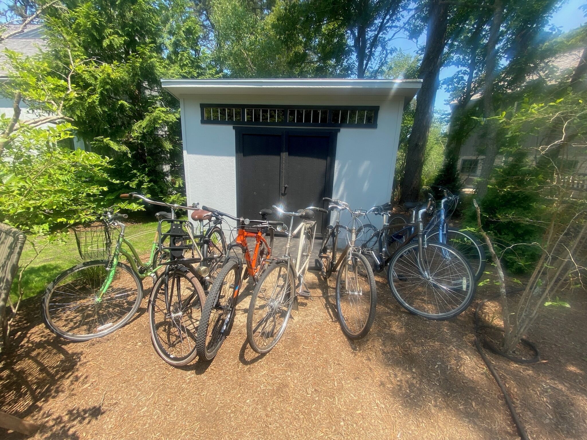 A small shed with a black door and windows, surrounded by bicycles.