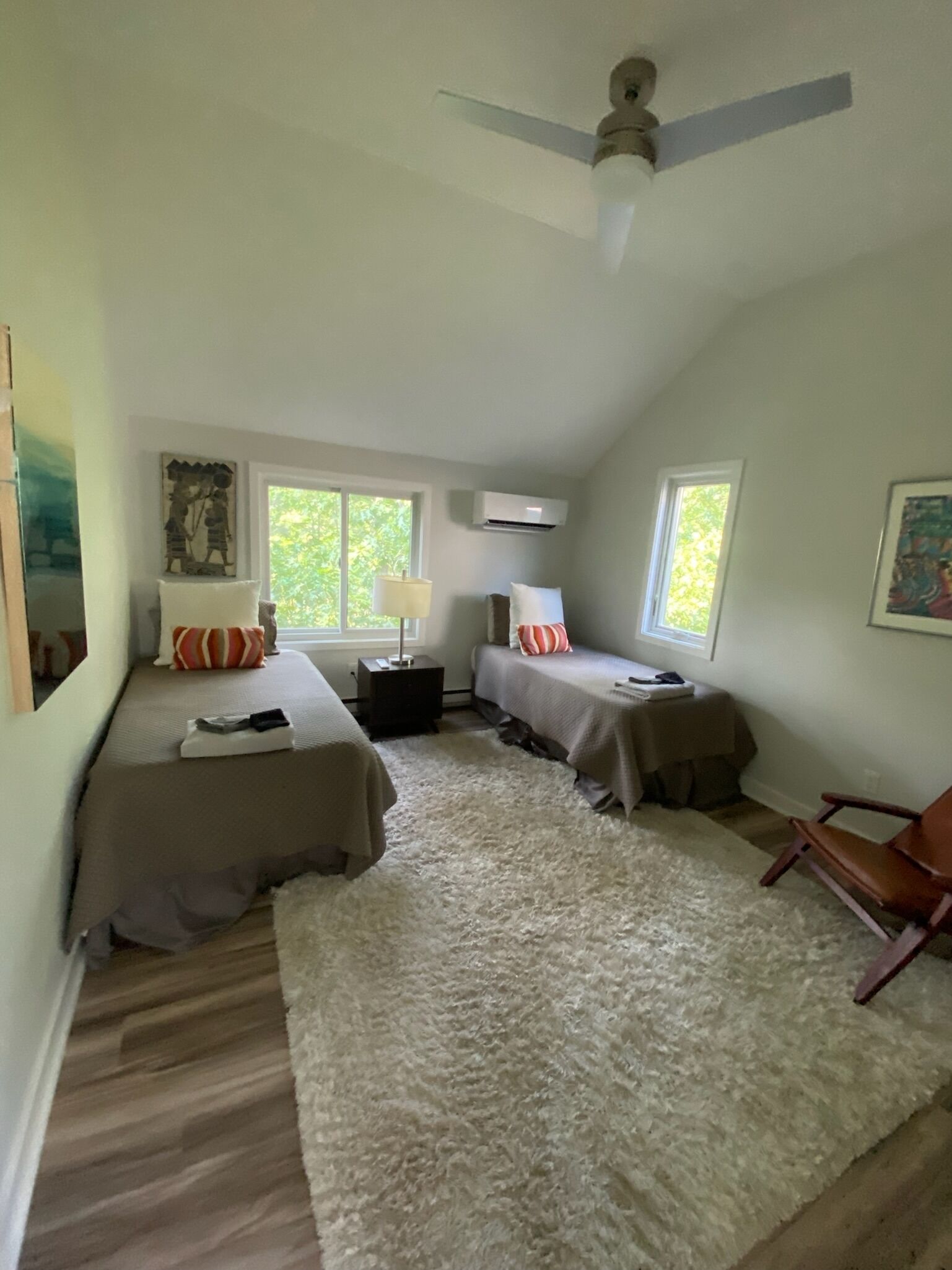 A bedroom with two beds, a ceiling fan, and a large window.