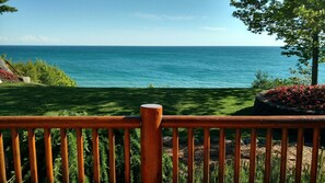 A wooden deck overlooking a coastal view with a grassy area and a flower bed. - Log Home on Lake Michigan (Brevort)