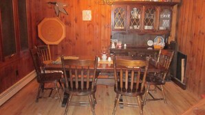 Une pièce aux murs lambrissés, avec une table à manger et quatre chaises. Un lustre est suspendu au plafond, et un buffet aux portes vitrées est adossé au mur.