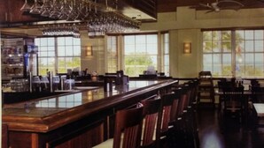 A bar area with a long counter, multiple chairs, and large windows allowing natural light.